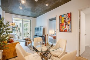 Ein modernes Wohnzimmer mit einem Glastisch, weißen Sofas, einem Fernseher und einem Balkon mit Blick auf ein Gebäude.