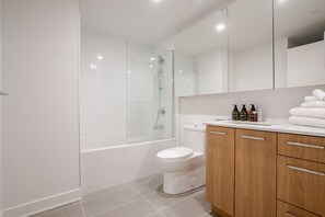 Ein modernes Badezimmer mit einer Glaskabine zur Dusche, einer weißen Toilette und Holzschränken.