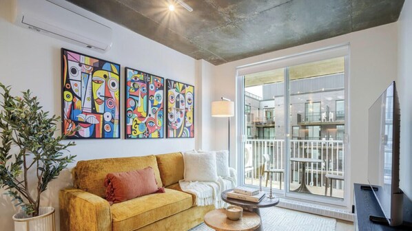 Ein Wohnzimmer mit einem gelben Sofa, einem Fernseher und abstrakten Bildern an der Wand.