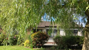 Uma casa com telhado em telhas, rodeada por um jardim bem cuidado com arbustos variados e gramado.