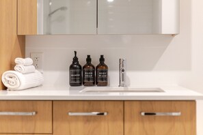 A bathroom with a white countertop, three bottles of personal care products, and a towel. - Montreal Retreat with Rooftop Pool & Parking (Montreal)