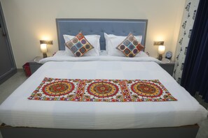 Uma cama com colcha branca, duas almofadas decorativas e um cobertor estampado.
