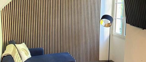 A modern living room with a sectional sofa, a small wooden stool, a floor lamp, and a sloped ceiling with vertical wooden panels.