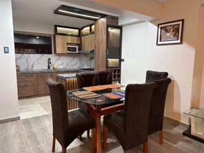 Une cuisine moderne avec des meubles de couleur bois foncé, un four à micro-ondes encastré et une table à manger en verre, assortie de chaises marron.