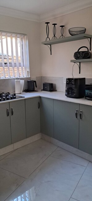 A kitchen with grey cabinets, a gas stove, a kettle, a toaster, and a radio on a shelf. - Luxury Guest Apartment Fully Furnished With all Amenities (Pretoria)