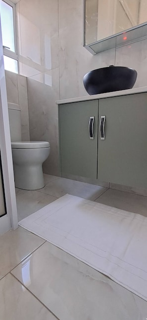 Une salle de bain avec des toilettes, un meuble avec des poignées et un sol réfléchissant.