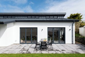Una casa moderna con un patio, una mesa de comedor con sillas y un ventanal corredero.