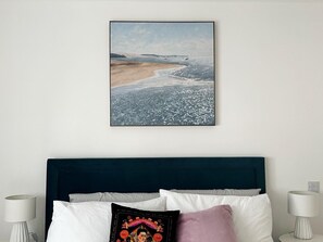 Une chambre à coucher avec un lit, des oreillers, une tête de lit et un tableau accroché au mur.