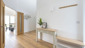 Una habitación con suelo de madera, un escritorio con cajones, un banco, un estante en la pared y una puerta que da a otra habitación.