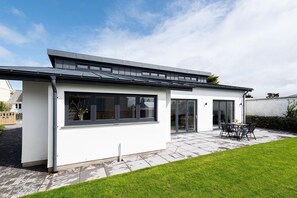 Une maison moderne dotée d’un patio, d’un espace salon extérieur abrité et d’une grande fenêtre.