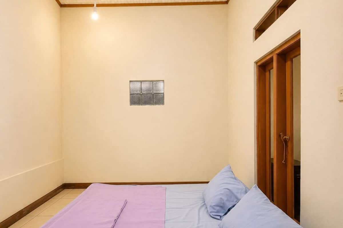 Ein Zimmer mit einem Bett, einem kleinen Fenster und einer Tür.