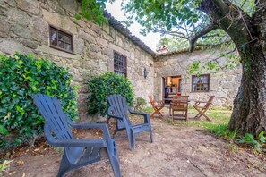 Un edificio de piedra con fachada rústica, un pequeño comedor con muebles de madera y dos sillas de plástico al frente.