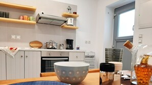 Een keuken met witte kastjes, een fornuis, een koffiezetapparaat en een raam.
