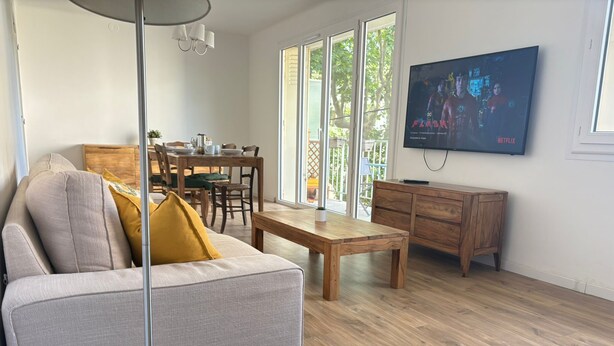 Ein Wohnzimmer mit einer Couch, einem Couchtisch, einem Fernseher und einem Essbereich mit Stühlen und Tisch.
