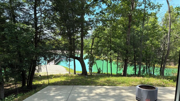 A concrete patio area with a cylindrical object, surrounded by trees and a body of water. - Gated Luxury Glamping at Diamond Acres – Near Grove Marina & Cumberland Falls (Corbin)