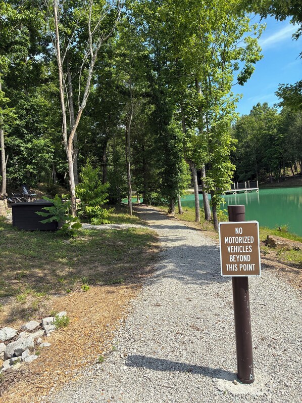 A gravel path leading to a lake, surrounded by trees, with a sign prohibiting motorized vehicles beyond a certain point.