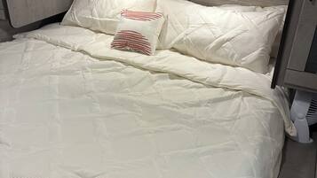 A bed with a quilted white cover and two pillows, one with red stripes.