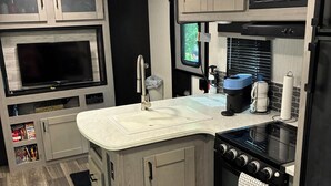 A compact kitchen with a built-in TV, a coffee maker, and a stove. - Gated Luxury Glamping at Diamond Acres – Near Grove Marina & Cumberland Falls (Corbin)