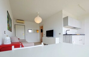 A modern living room with a sofa, a television, and a kitchen area with cabinets and a sink. - BEst16 Relax&SeaView. Seafront, with covered parking space. (SAN LORENZO AL MARE)