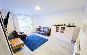 Un salon avec un canapé en cuir marron, un tapis bleu, un meuble en bois et un téléviseur.