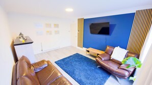 En moderne stue med sofa, sofabord, fjernsyn og en blå væg.