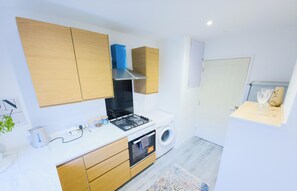Une cuisine compacte équipée d’une cuisinière, d’un four et d’un lave-linge, de placards en bois et d’un petit plan de travail.