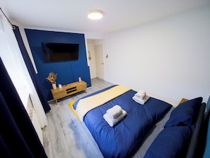 Ein Schlafzimmer mit einem Bett, einem Fernseher an der Wand, einem Holznachttisch und einer Tür.