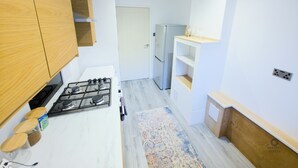 Et kompakt køkken med gasblus, træskabe, et indbygget køleskab og en lille hylde med vinglas.