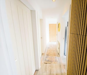 Un couloir avec un plancher en bois, des murs blancs, une porte et un radiateur.