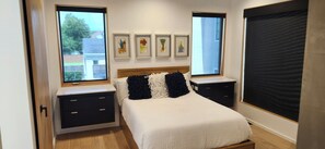 Ein Schlafzimmer mit einem Bett, zwei Nachttischen, einem Fenster und Wandbildern.