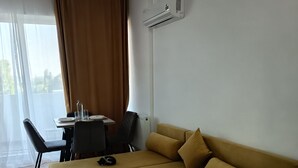 A modern living room with a sectional sofa, a dining table with chairs, and an air conditioning unit on the wall. - Roma Apartment luxury flat in a beautiful location in Mamaia Beach by the Sea. (Năvodari)