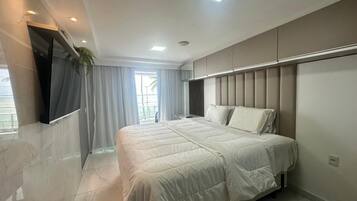 Une chambre moderne avec un grand lit, un téléviseur fixé au mur et une fenêtre avec des rideaux.