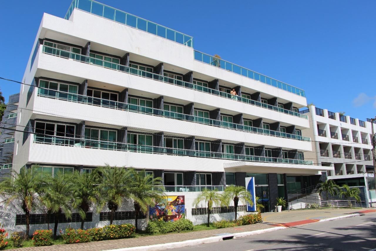 Un immeuble à plusieurs étages doté de balcons, d’une entrée principale et d’un espace paysager agrémenté de palmiers.