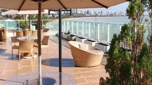 An outdoor patio with wicker furniture, a glass table, and a large umbrella. - Blue Sunset Cabo Branco | Beachfront Apartment (João Pessoa)