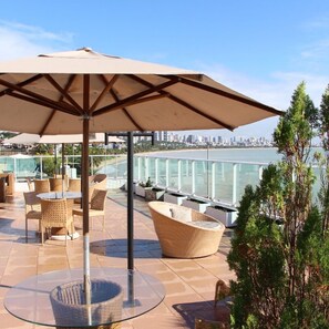 An outdoor patio with wicker furniture, a glass table, and a large umbrella. - Blue Sunset Cabo Branco | Beachfront Apartment (João Pessoa)