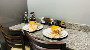 A dining table with two plates of food, a coffee mug, and a decorative sign. - Blue Sunset Cabo Branco | Beachfront Apartment (João Pessoa)
