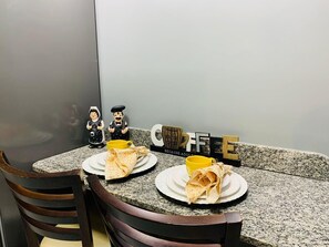 A dining table with two plates of food, a coffee mug, and a decorative sign. - Blue Sunset Cabo Branco | Beachfront Apartment (João Pessoa)