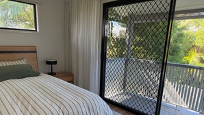 A bedroom with a bed, nightstand, and a view through a balcony door. - Beach Stay | Walk to the Surf, Café & Shops (Coolum Beach)
