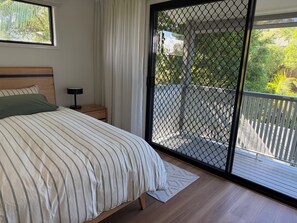 Ein Schlafzimmer mit einem Bett, einem Nachttisch und Blick durch eine Balkontür.
