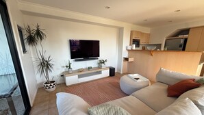 A modern living room with a flat-screen TV, a sofa, a coffee table, and a potted plant. - Beach Stay | Walk to the Surf, Café & Shops (Coolum Beach)