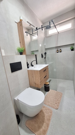 A modern bathroom with a white toilet, wooden vanity, and a glass shower enclosure.. Apartman Pino Charming 1-bedroom apartment in Bihać