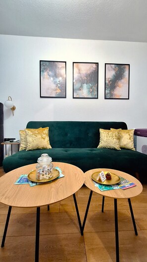 Een woonkamer met een groene bank, twee ronde houten tafels en drie abstracte schilderijen aan de muur.