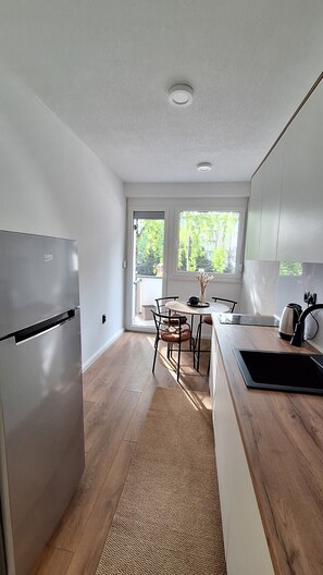A modern kitchen with a built-in refrigerator, a dining area with a table and chairs, and a large window providing natural light. - Apartman Pino Charming 1-bedroom apartment in Bihać (Bihać)