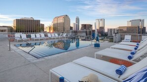 Piscina no terraço com espreguiçadeiras e vista para a paisagem urbana.