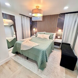 A modern bedroom with a large bed, bedside tables, a bench, a mirror, and a wall-mounted light fixture. - Luxe 3BR w/Private Bath in Every BR Near Airport (Newark)