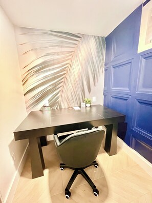 A modern office space with a dark table, a green office chair, a decorative leaf wall, and a blue door. - Luxe 3BR w/Private Bath in Every BR Near Airport (Newark)