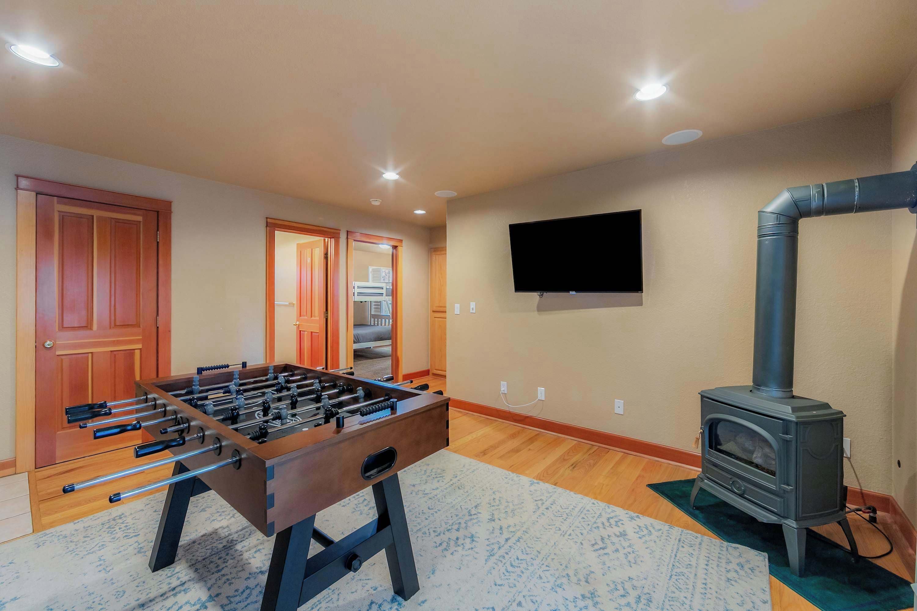 A room with a foosball table, a television mounted on the wall, and a wood-burning stove.