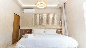 Ein Hotelzimmer mit einem großen Bett, einer Deckenleuchte, einer wandmontierten Klimaanlage und einer Holztür.