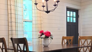 Een eetkamer met een donker houten tafel, vier houten stoelen, een kroonluchter en een vaas met bloemen.