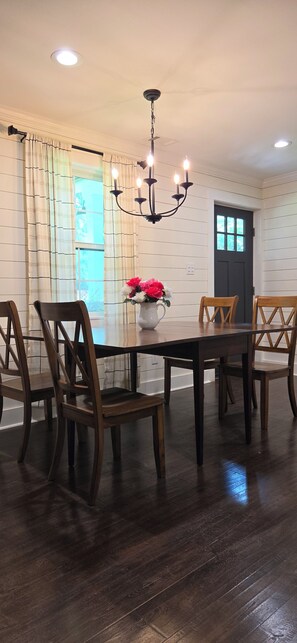 A dining room with a dark wooden table, four wooden chairs, a chandelier, and a vase with flowers.